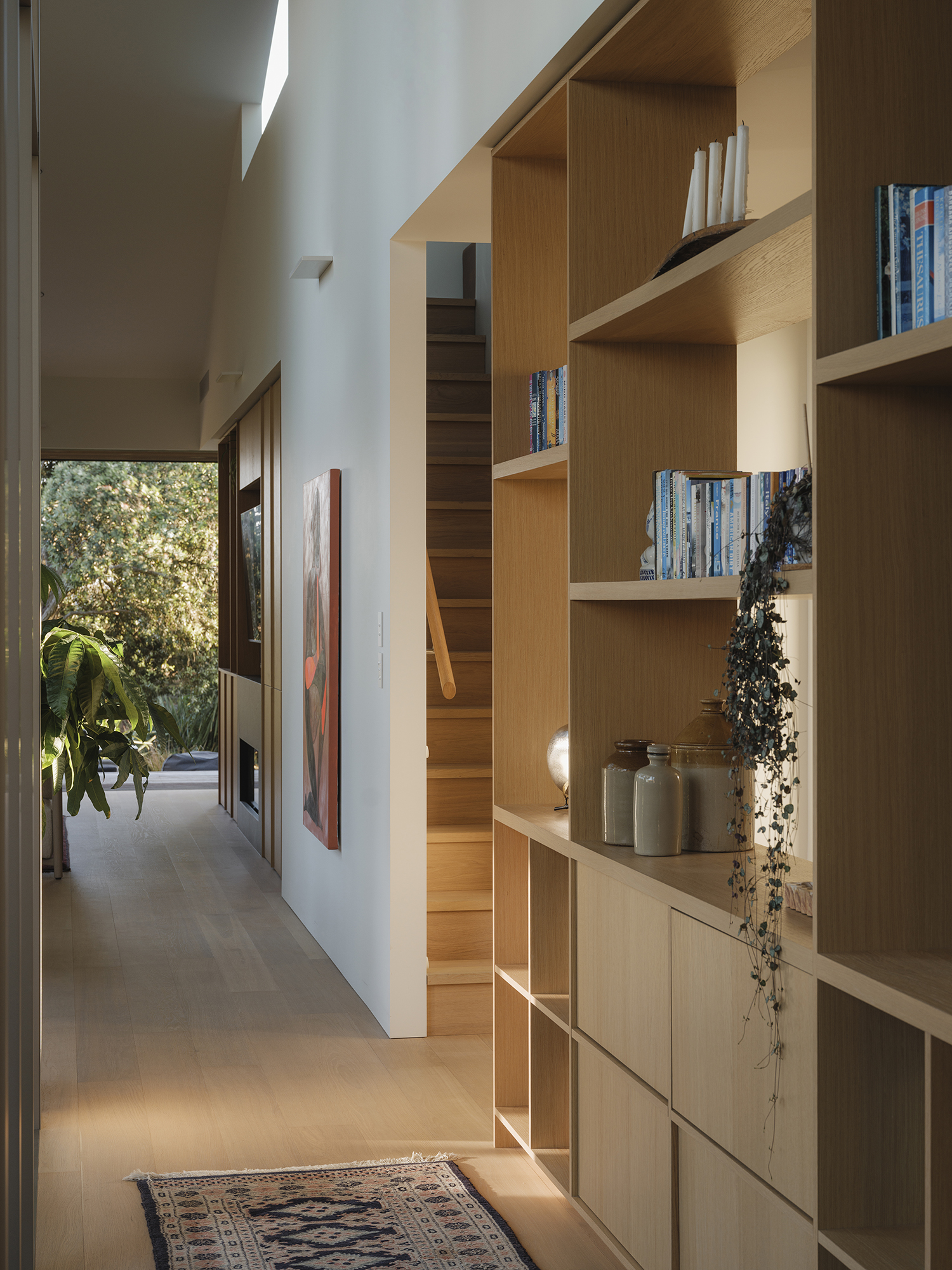 Treefold central spine — oak joinery wall with built-in shelving and considered detailing, view through to the garden