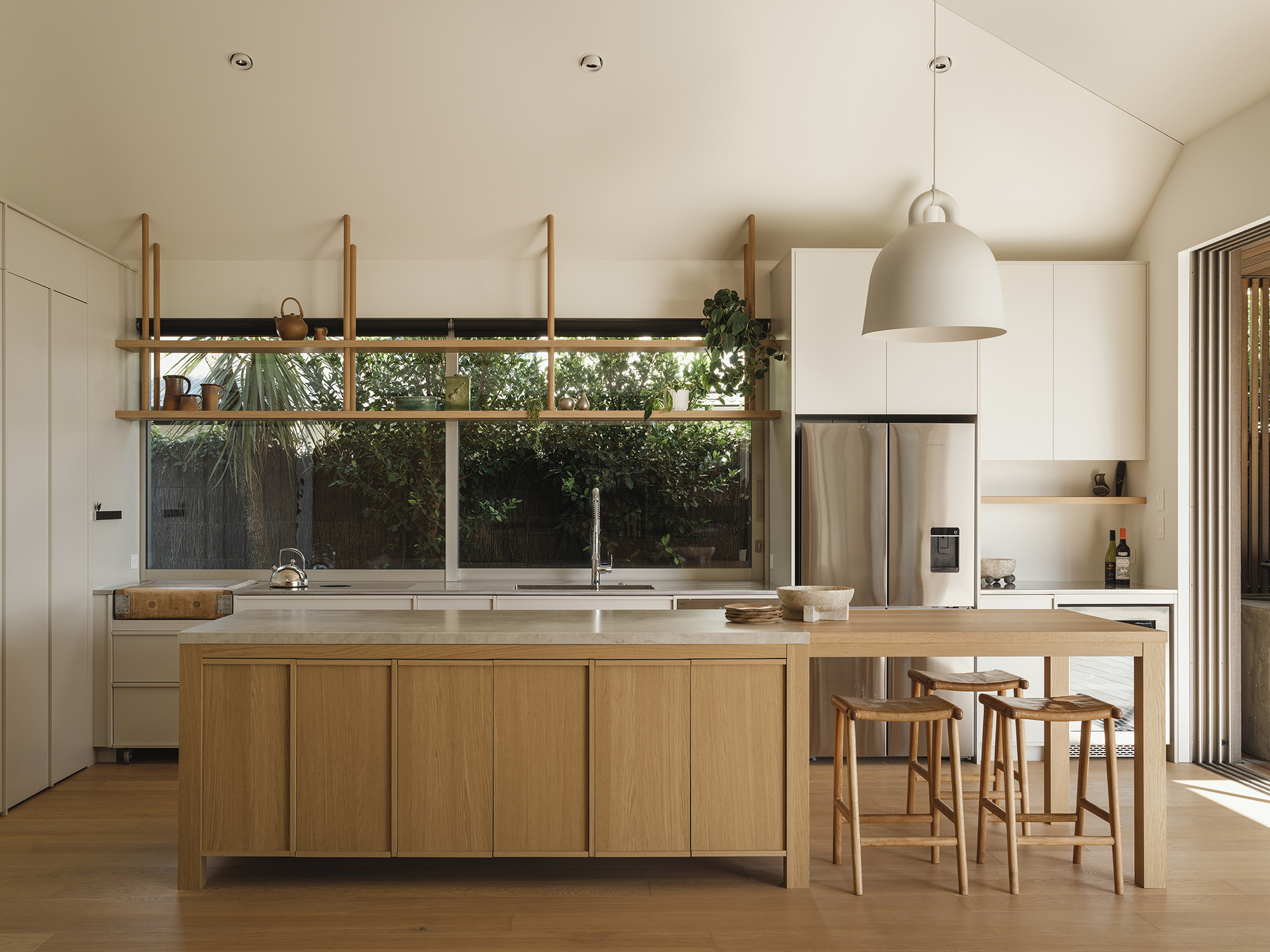 Treefold kitchen — light oak island and joinery beneath a vaulted ceiling, low ribbon window framing the garden