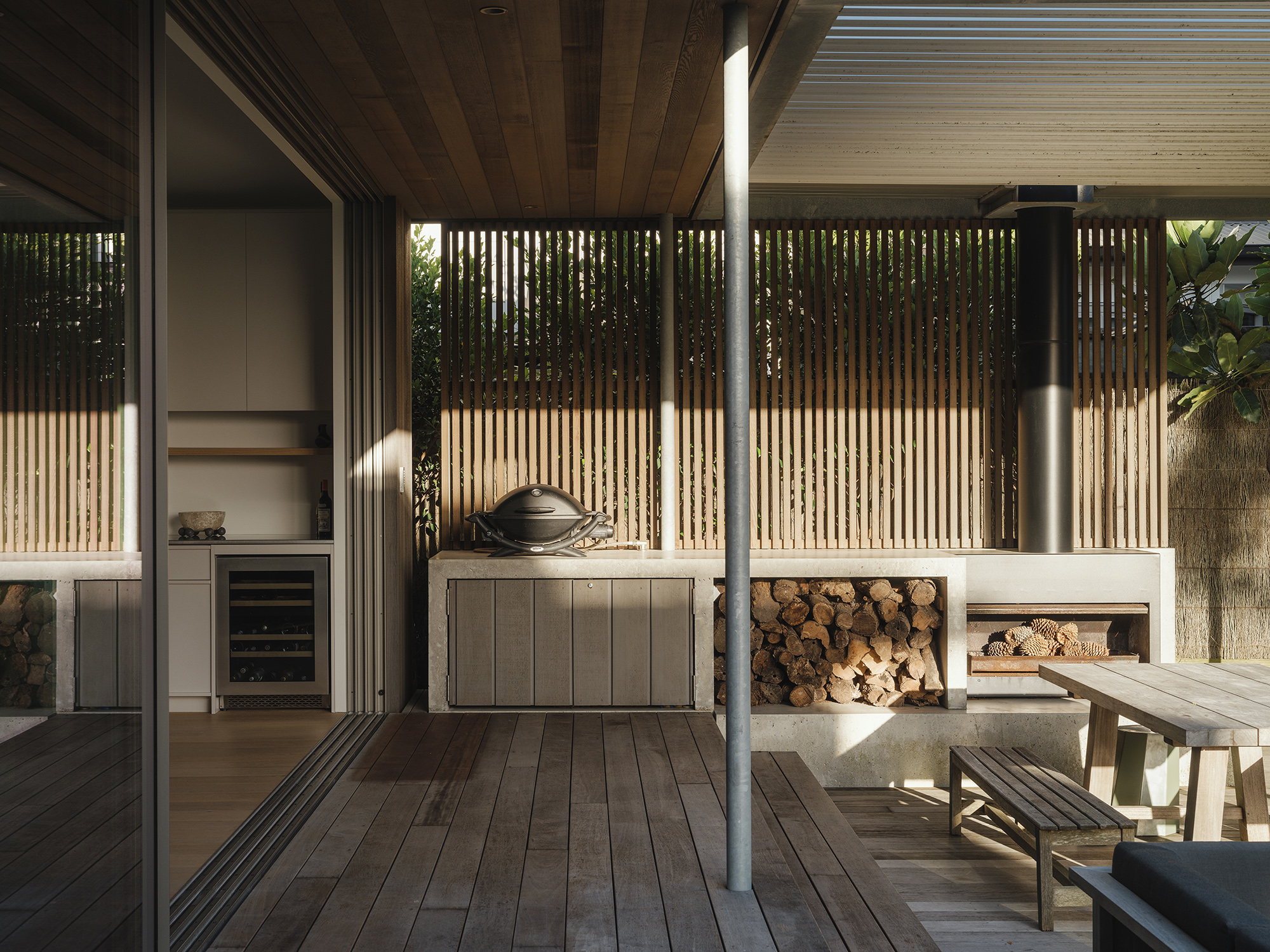 Treefold outdoor room — sheltered covered deck with timber screens, fireplace and stacked firewood, demonstrating year-round passive use